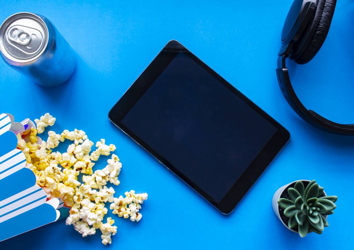 A photo of pop and popcorn laid out on a blue table with a tablet and headphones ready to entertain