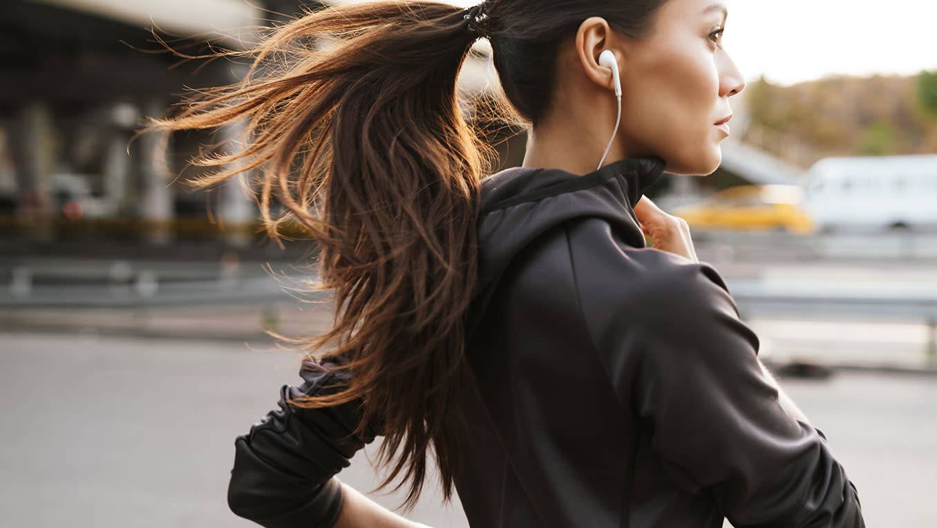 A woman of colour jogs through the city, listening to content with earbuds