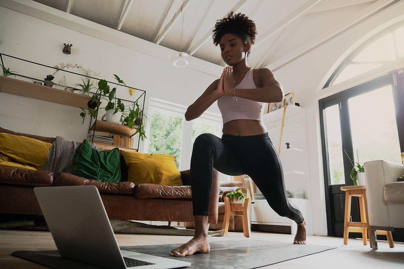 Woman in standing lunge with hands in prayer position, on yoga mat in living room