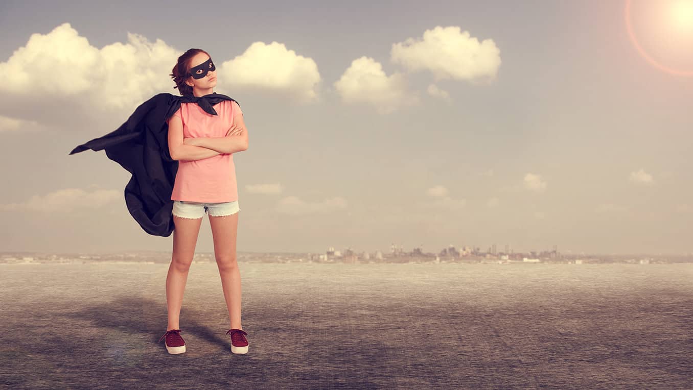 Young adult dressed as a super hero stands on a flat field with the sun rising in the background