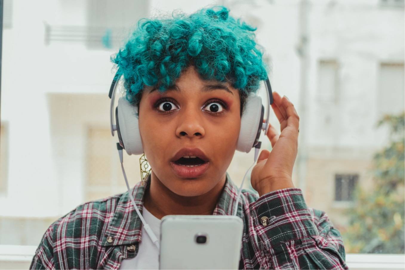 A young woman with teal hair has a fright while listening to audio content on her headphones