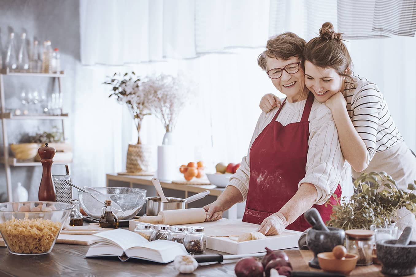 An adult woman and her elderly mother bond happily over a baking recipe, with rolling pin at the ready