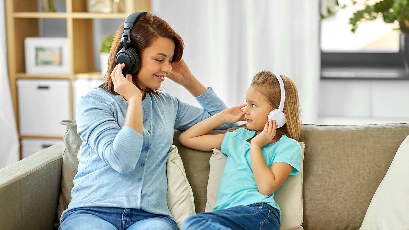 Mother and daughter sitting together on a sofa listening to a children's audiobook at home