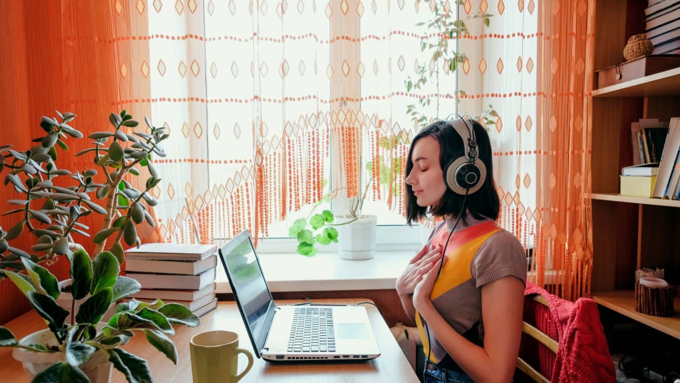 A white woman in headphones listens peacefully to audio content on a laptop