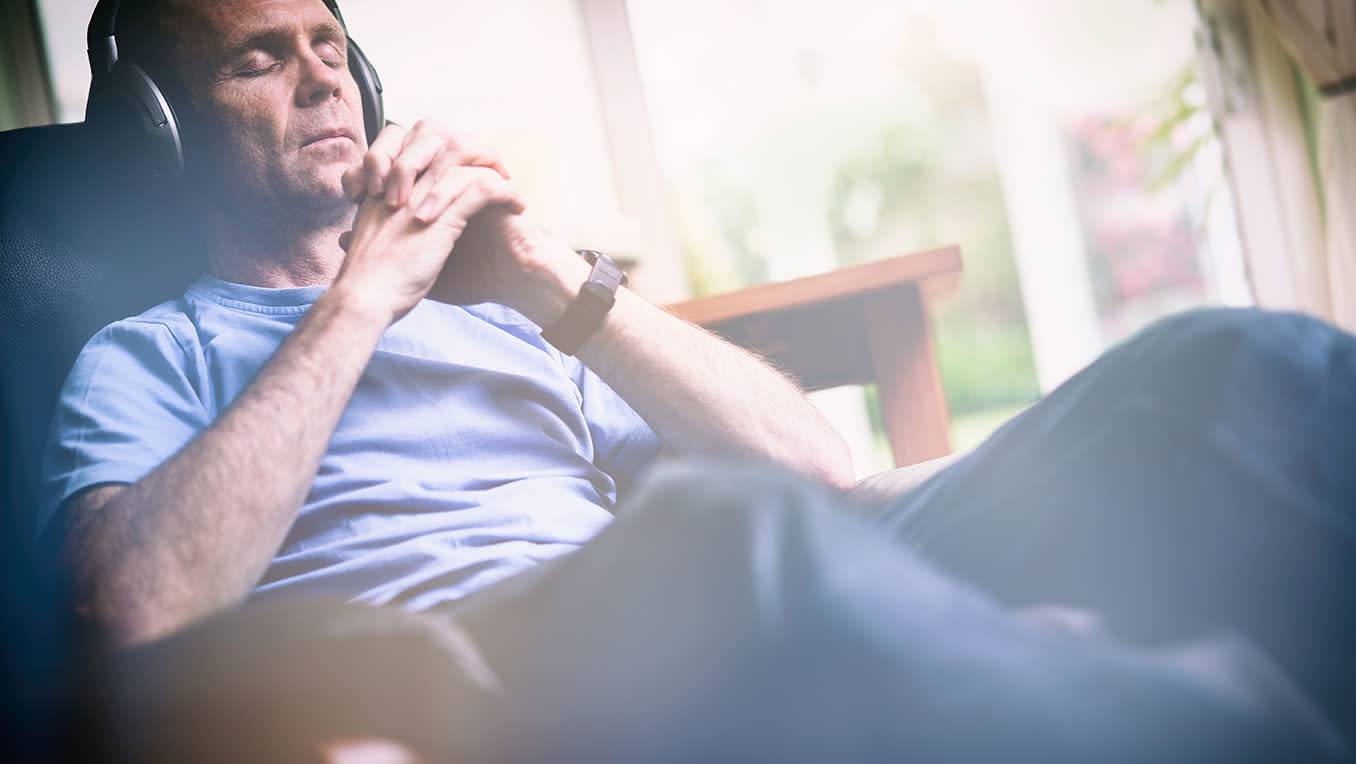 An elderly White man sits contentedly with his eyes closed listening to audio content 