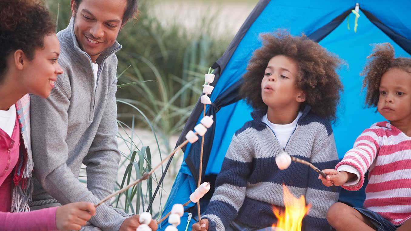 An African American family are camping, roasting marshmallows over a campfire