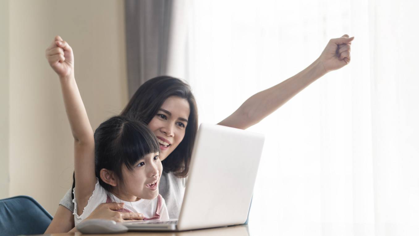 An Asian mother and her daughter engage in excitement with audio content on a laptop