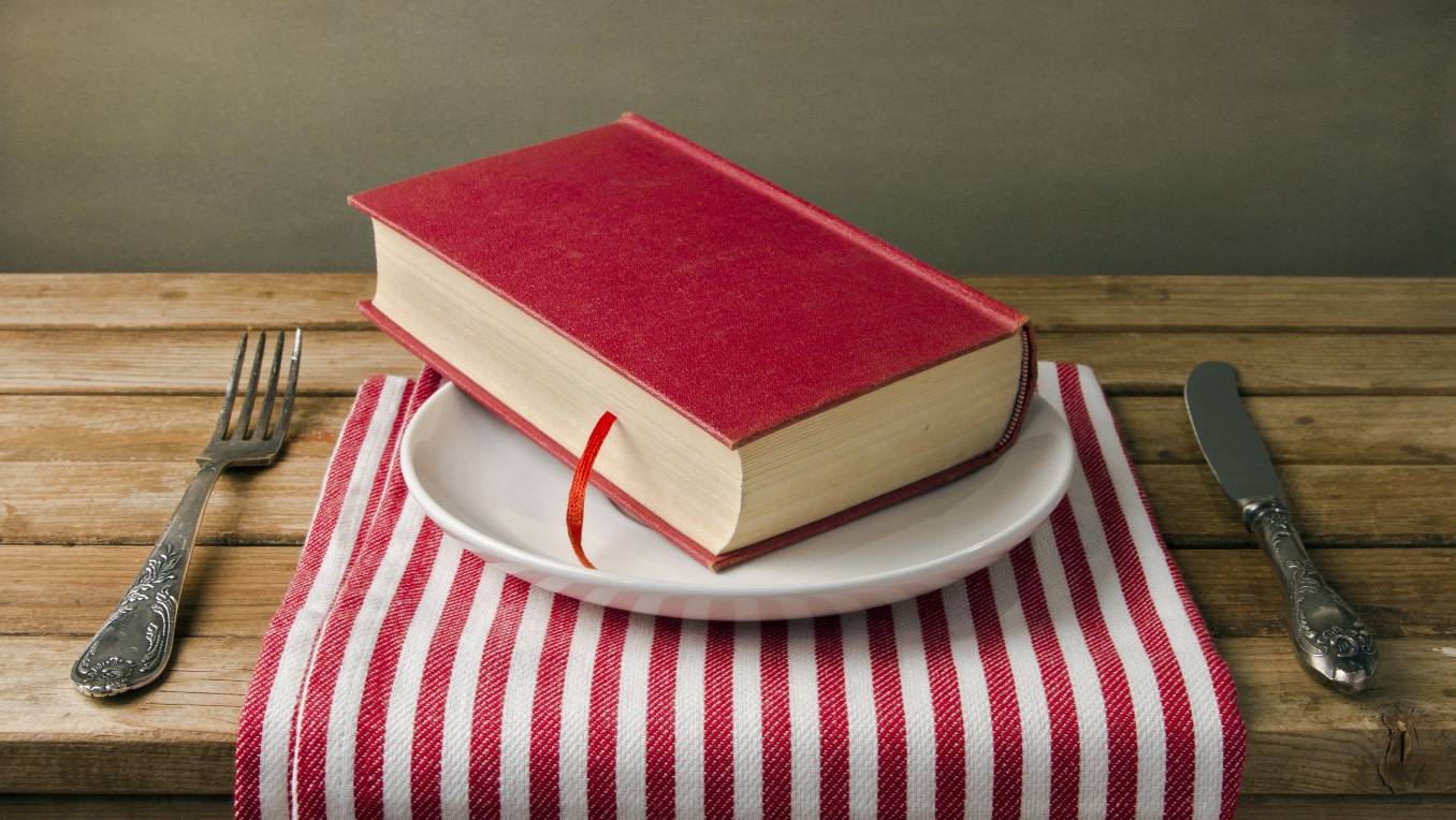 A photo of a place setting with a napkin, a knife and fork and a book atop the plate