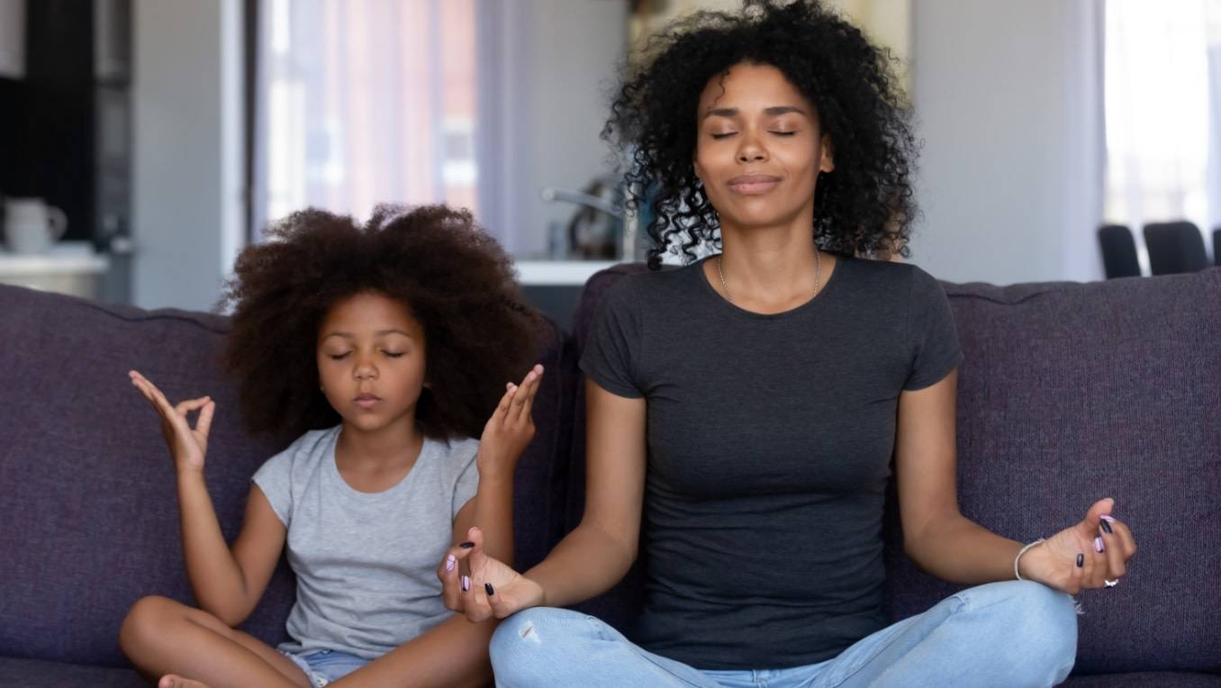 A mother and daughter contentedly meditate on the couch