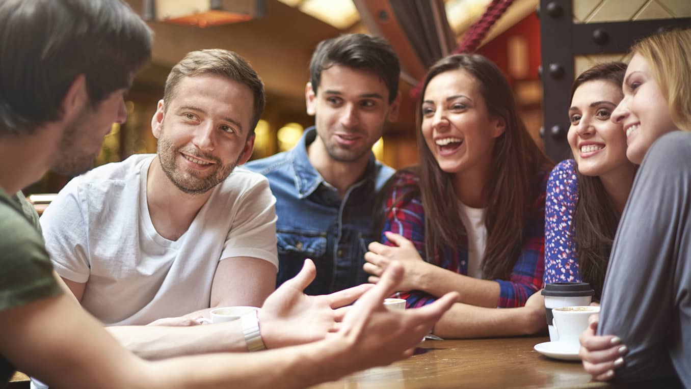 Group of friends sit together talking in conversation over coffee