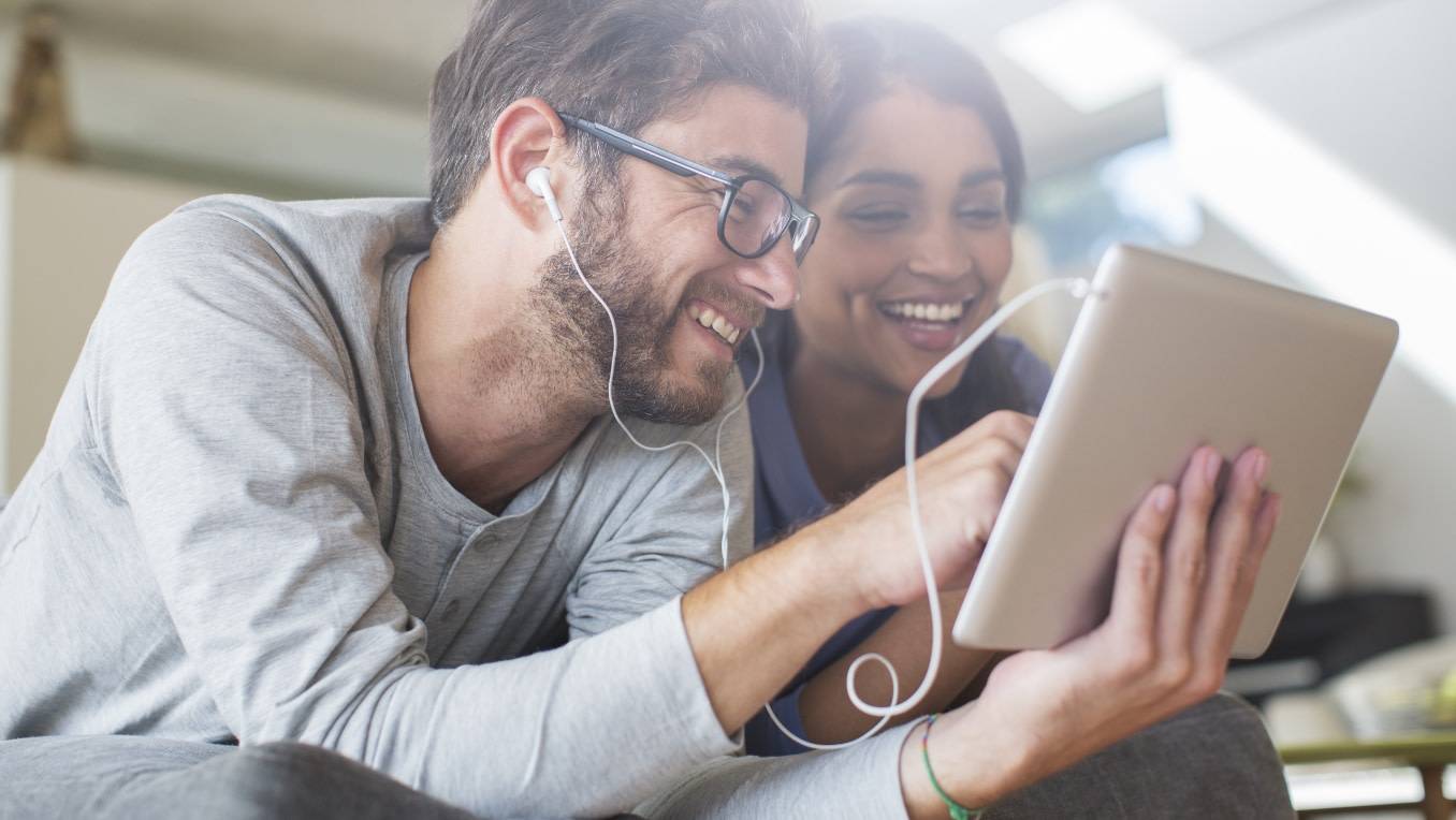 A couple shares headphones enjoying audible content together on a tablet