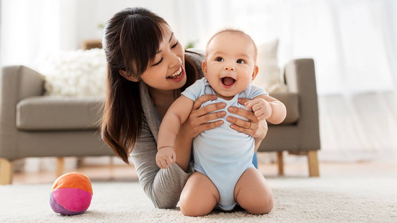 A mother playing on the living room floor with her laughing baby