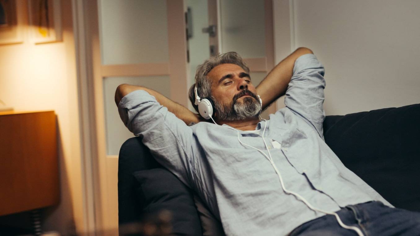 A middle-aged white man reclines in a chair enjoying audio content