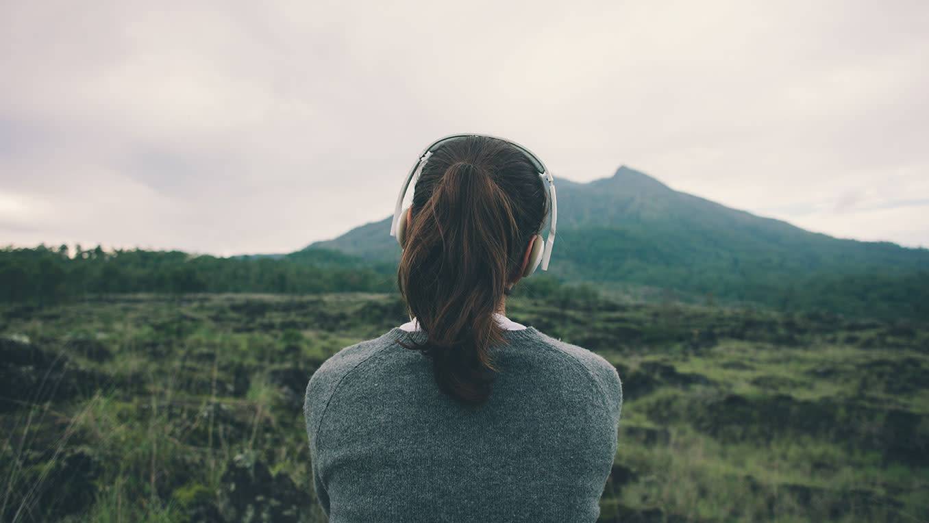 Traveler sitting on an open plain staring at a mountain peak in the distance while listening to audiobooks on her headphones