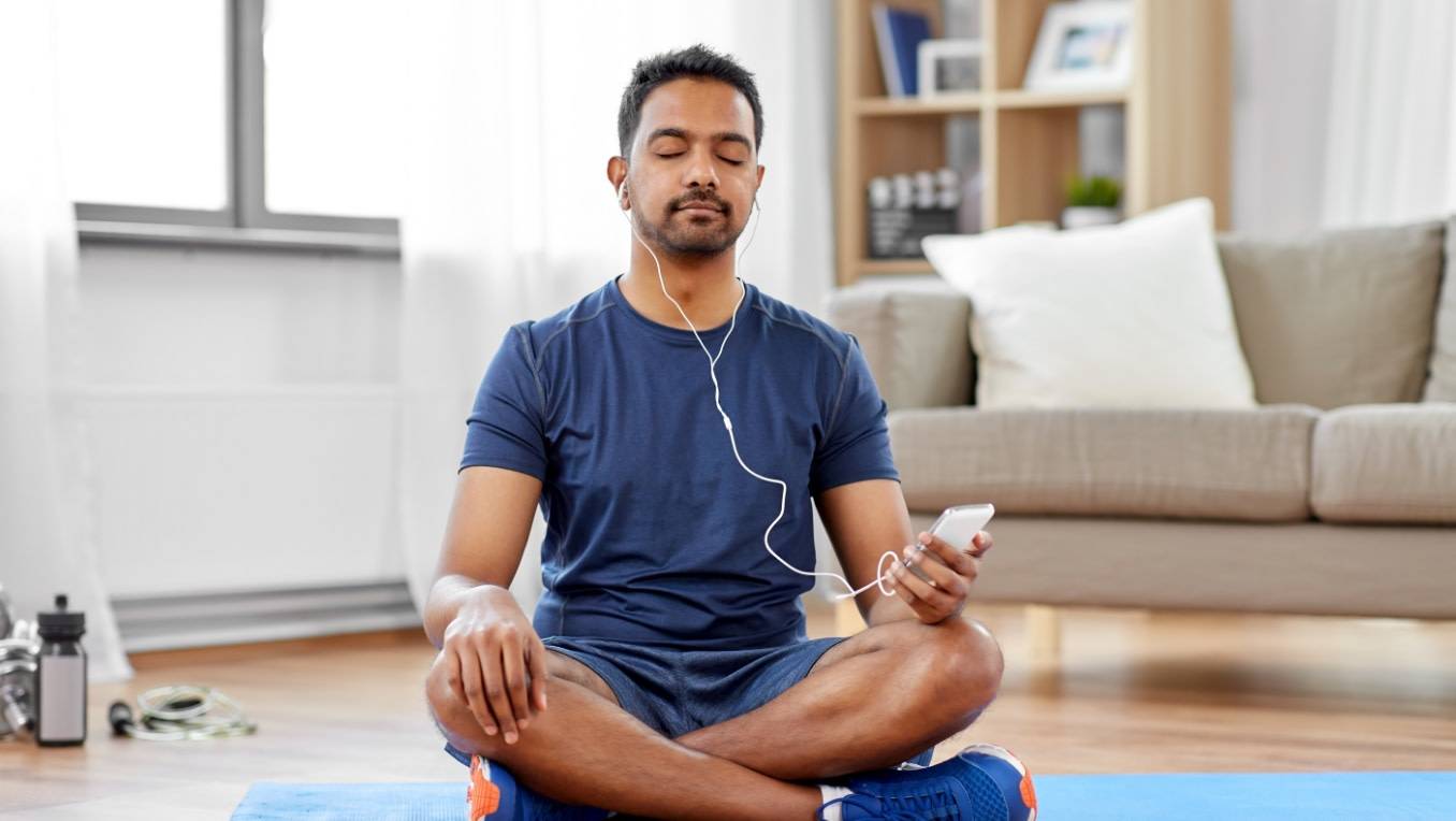 A man sitting on his yoga mat contentedly listens to an audiobook 