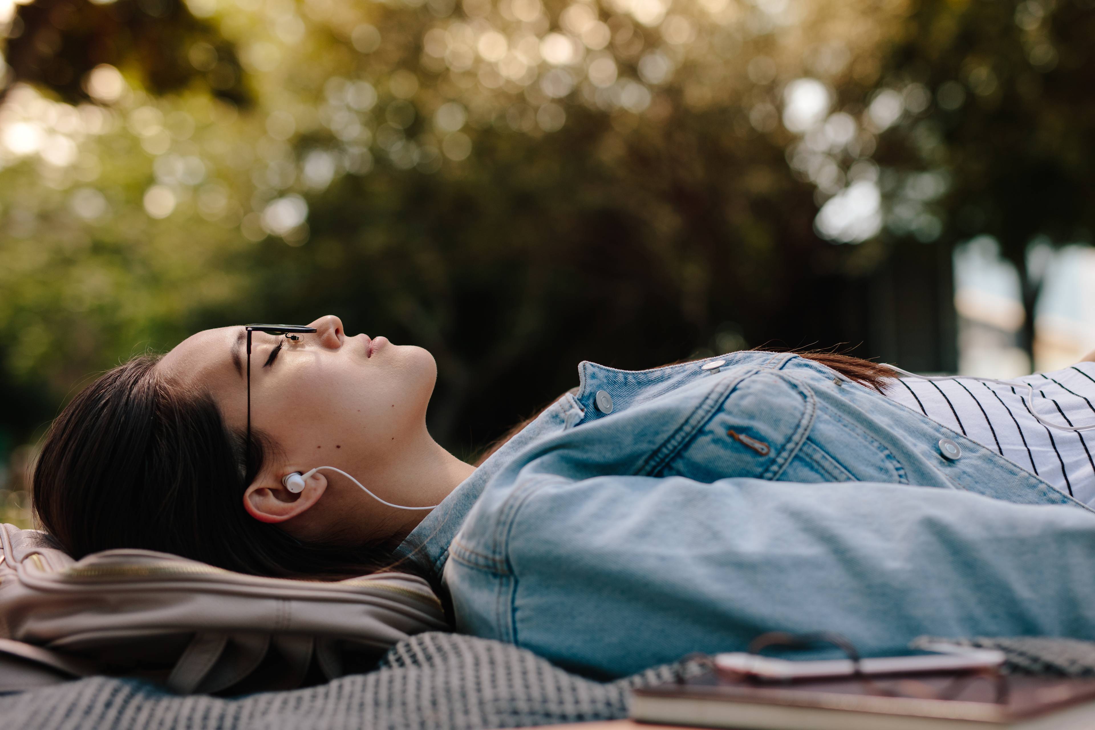 A young, Asian woman lies down listening contentedly to audio entertainment with earbuds